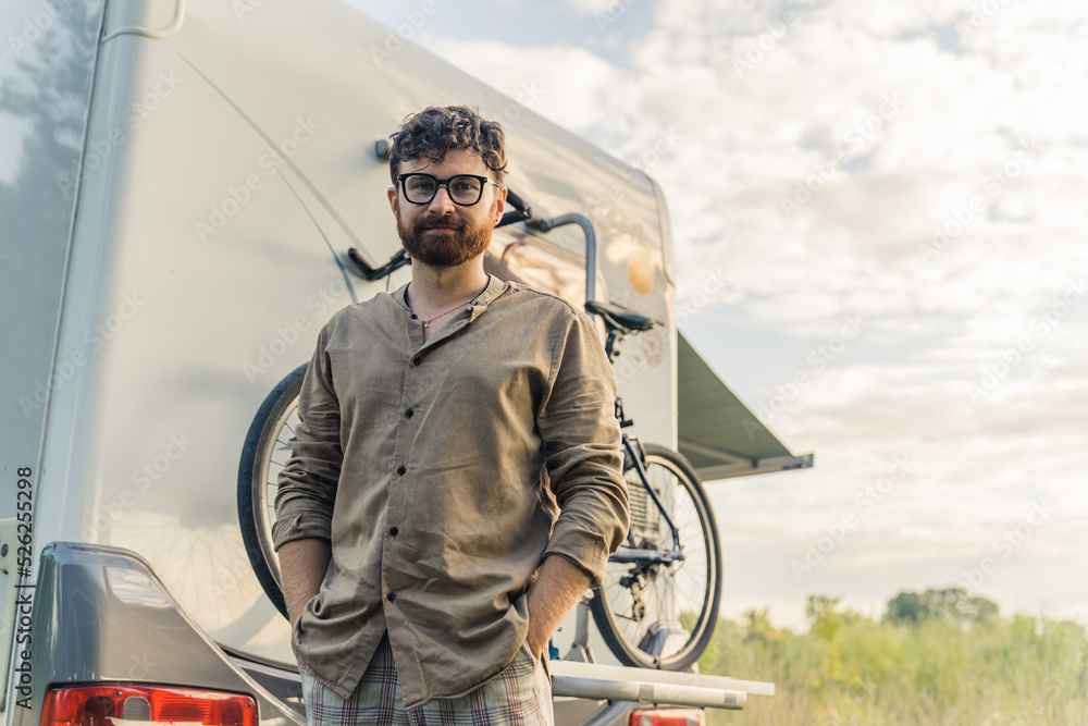 young Caucasian man with glasses standing behind the van, medium shot roadtrip concept. High quality photo