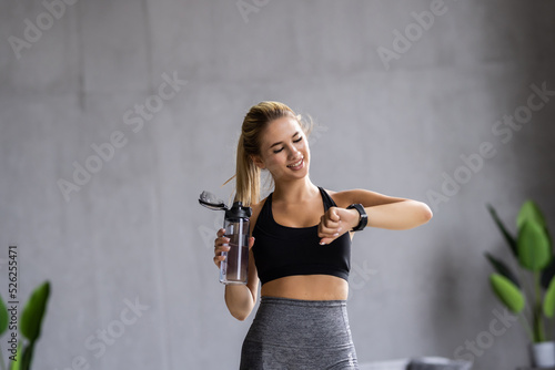 Pretty woman holding water looking at her smartwatch during doing yoga exercise at home