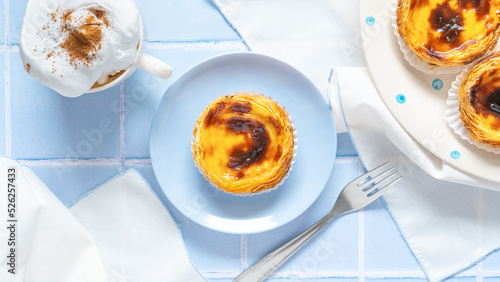 Traditional Portuguese egg tarts dessert Pasteis Pastel de nata or Pastels de Belem with a cup of capuchino coffee and forks on the blue tile. Flat lay