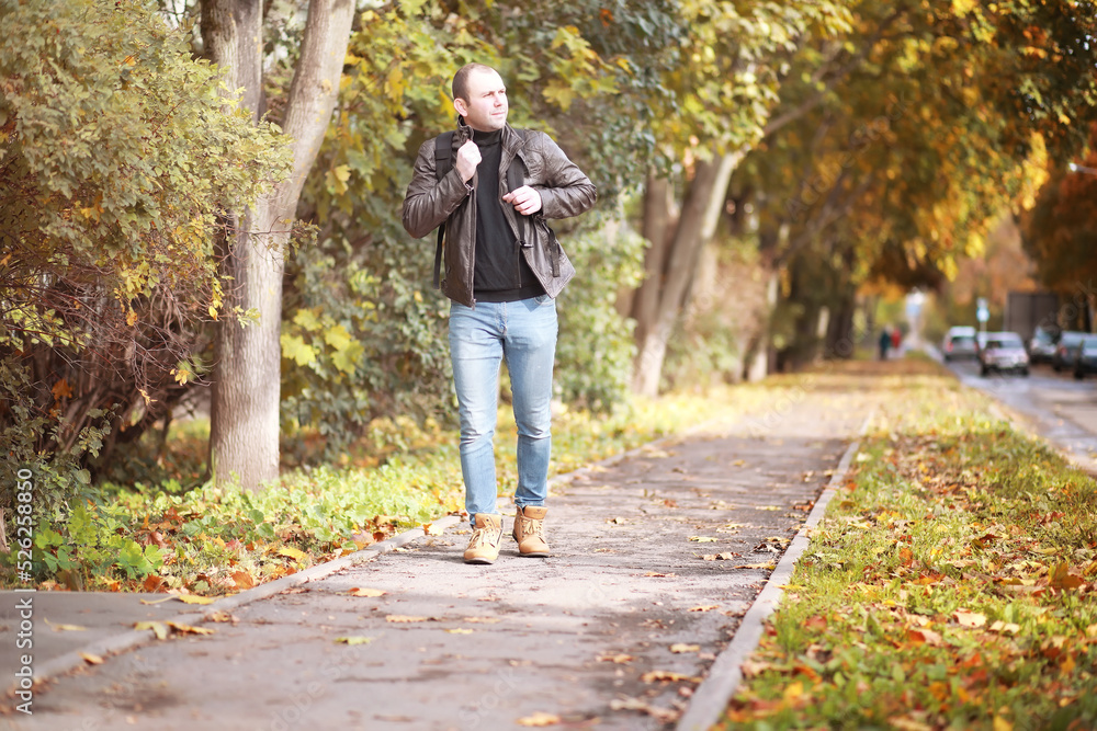 Fototapeta premium Autumn concept. A man walks through the city. Autumn leaves on the footpath.