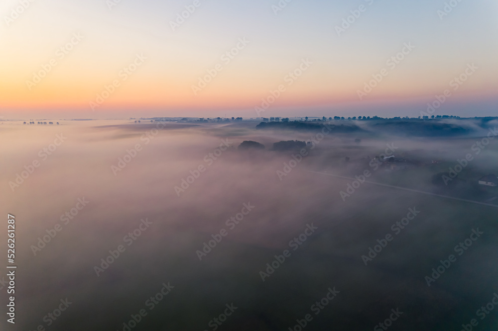 Birdseye view of farm fields in Roztocze Poland. Colorful sunrise and thick fog covering field. Trees in distance. Horizontal shot. High quality photo