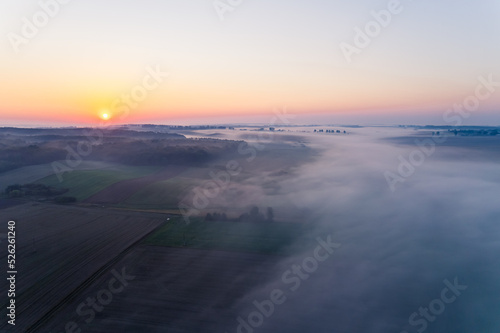 Bright orange rising sun and thick fog over colorful farm fields in Roztocze Poland. Morning views. Horizontal shot. High quality photo