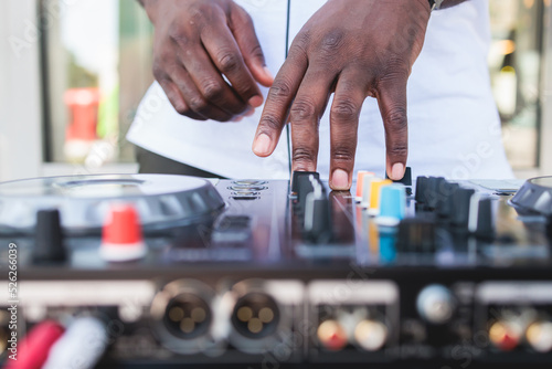 View of Dj mixer and vinyl plate with headphones on a table with african american DJ playing on stage and mixes the track in the background, during summer open air event techno party, hand close up © tsuguliev
