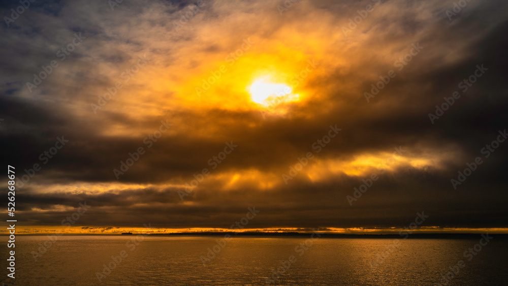 Golden Sun Rays behind Stormy Clouds at Sunrise over the Pacific Ocean