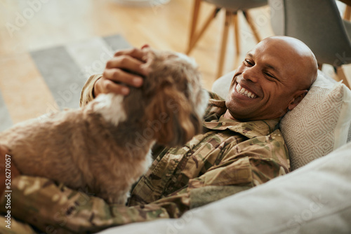 Happy African American military man enjoys with his dog at home.