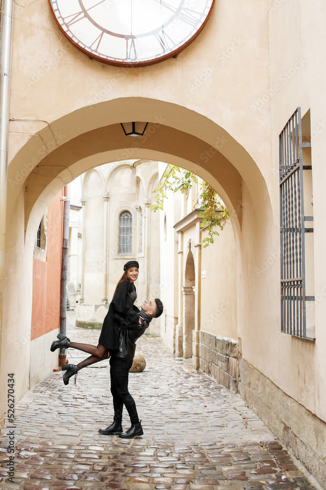 Stylish couple in the yard of the old town. The guy lifts the girl up, November 2, 2019, Lviv, Ukraine.