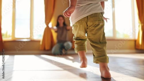 baby runs to mom at home. a child with bare legs runs across the floor to his mother against a sunny window. happy family kid dream concept. kid running back view at lifestyle home hugging mom