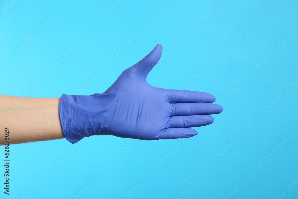 Person in medical gloves on light blue background, closeup of hand