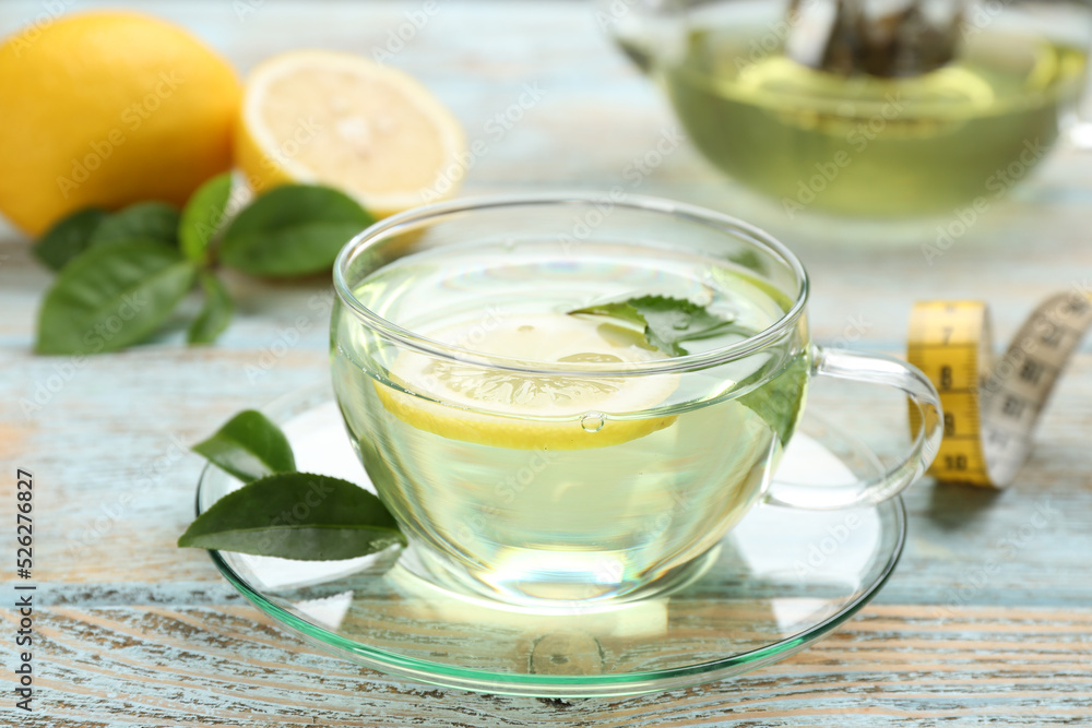 Glass cup of diet herbal tea with green leaves and lemon on wooden table Glass cup of diet herbal tea with green leaves and lemon on wooden table