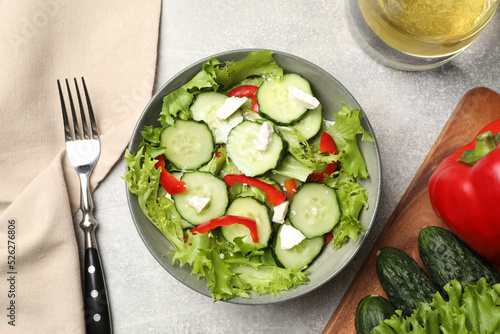 Delicious salad with cucumbers, red bell pepper and feta cheese in bowl served on light grey table, flat lay
