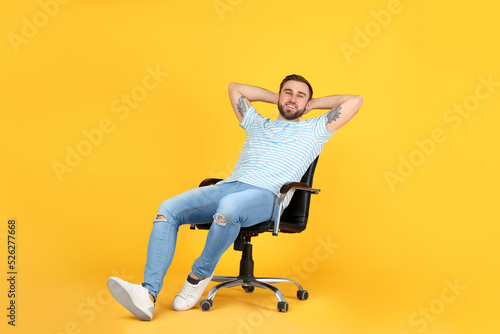 Fototapeta Naklejka Na Ścianę i Meble -  Young man relaxing in comfortable office chair on yellow background