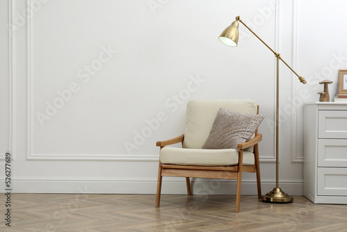 Stylish room interior with lamp, chest of drawers and armchair near white wall. Space for text