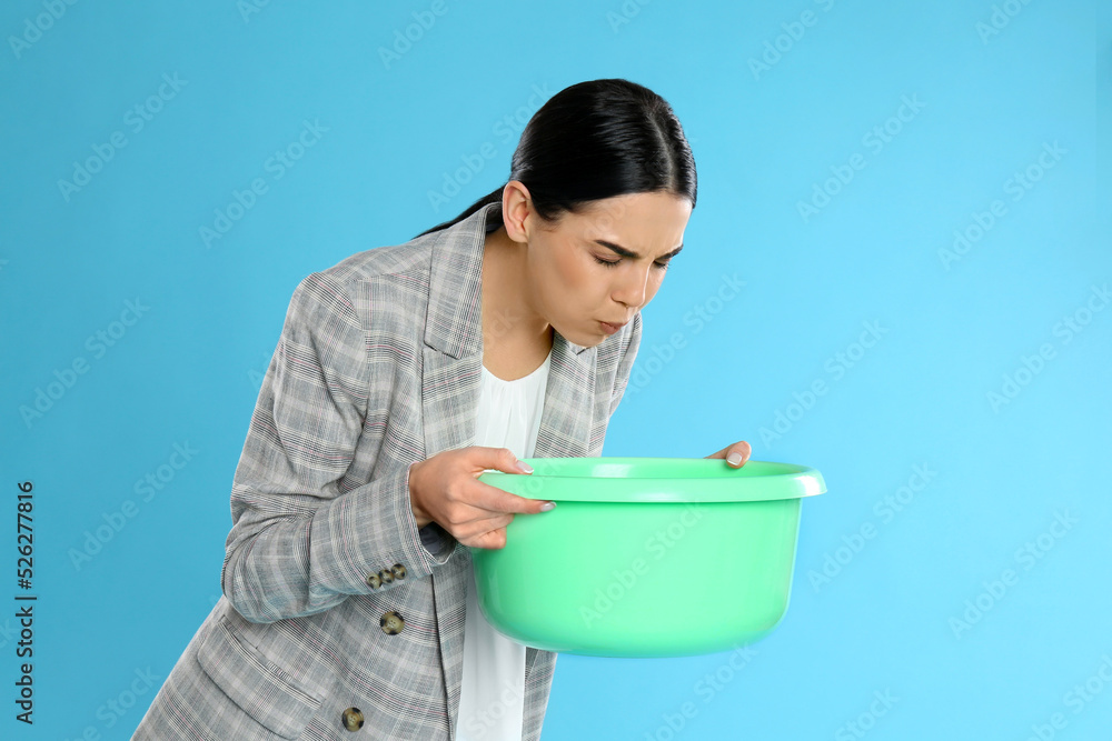 Woman with basin suffering from nausea on light blue background. Food poisoning