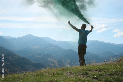 Man holding green smoke bomb in mountains