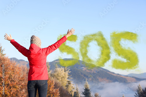 Woman and word SOS made of color smoke bomb in mountains  back view