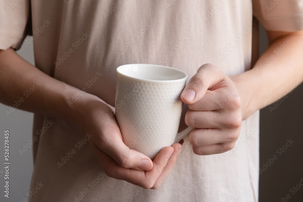 Mug in hands close-up. A young guy without a face in a light T-shirt holds a white mug. Mug in hands close-up. A young guy without a face in a light T-shirt holds a white mug.