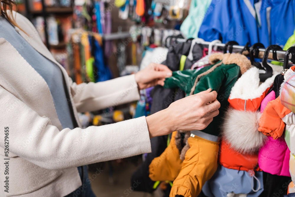 Cropped view of woman choosing animal jackets in blurred pet shop