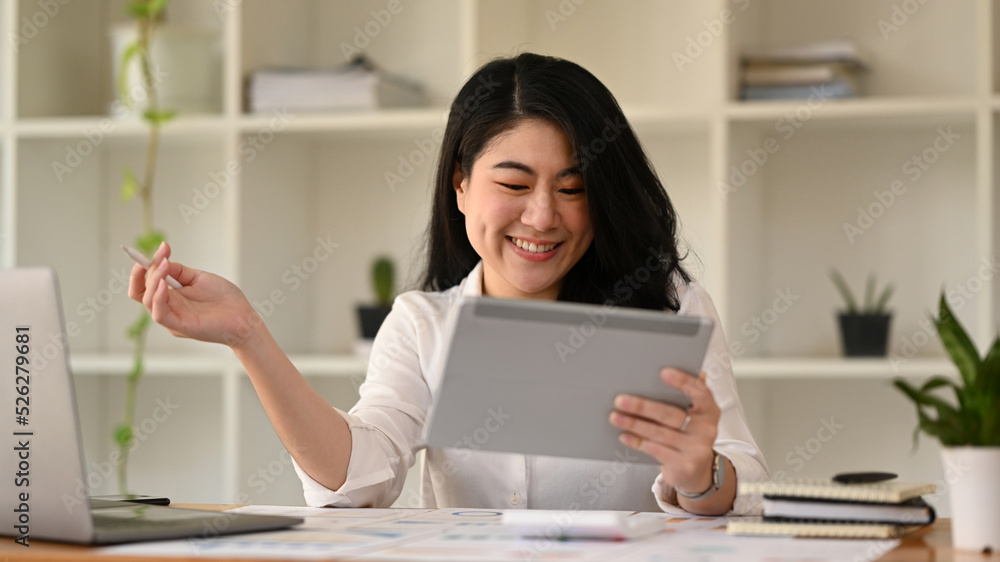 Successful asian woman entrepreneur using digital tablet and working with financial document at contemporary workplace