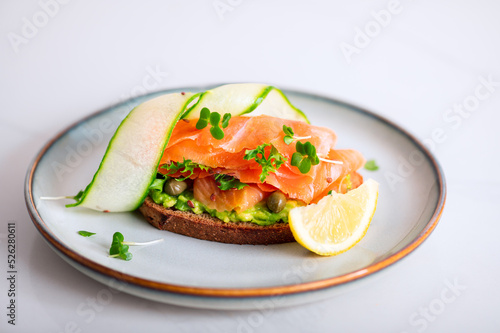 Toasted bread with mashed avocado, cucumber and smoked salmon on grey plate