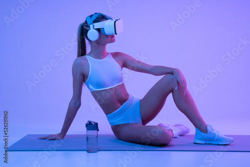Woman in training in metaverse under neon light on mat in vr glasses watching immersive tutorial