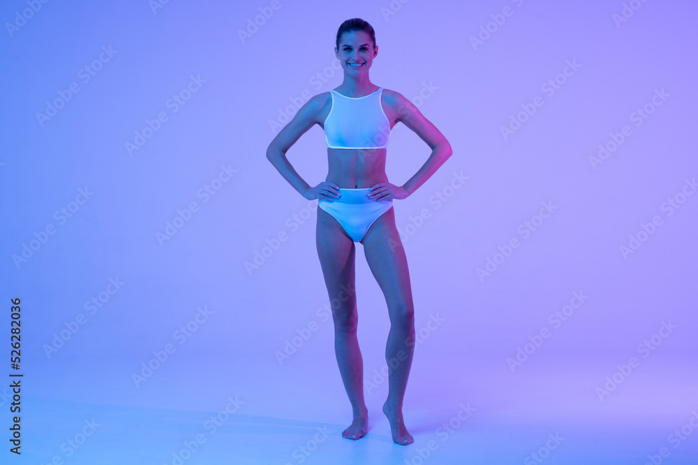 Full length shot of fitness woman posing in blue neon light with hands on waist