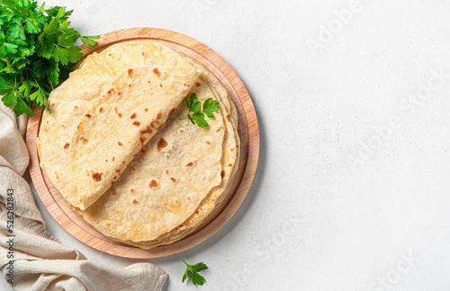 Traditional Indian chapati cakes on a wooden board with fresh herbs on a gray background. Top view, copy space