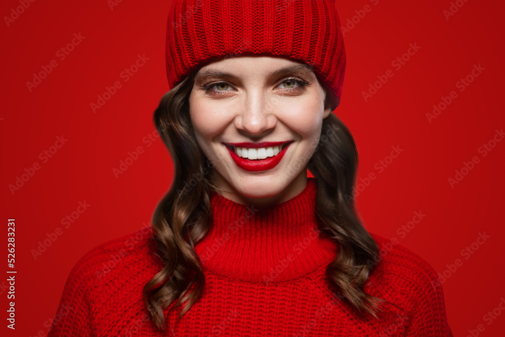 Close-up portrait of woman in christmas sweater and winter hat isolated on red background Close-up portrait of woman in christmas sweater and winter hat isolated on red background