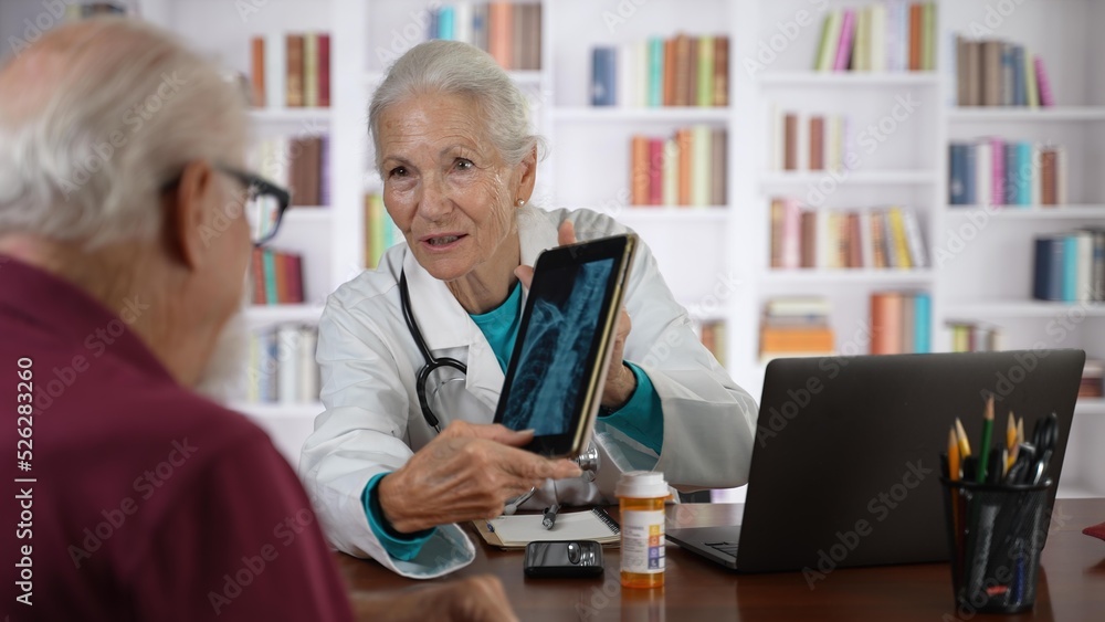 Elderly man consults with woman doctor looking at tablet computer showing x-ray.