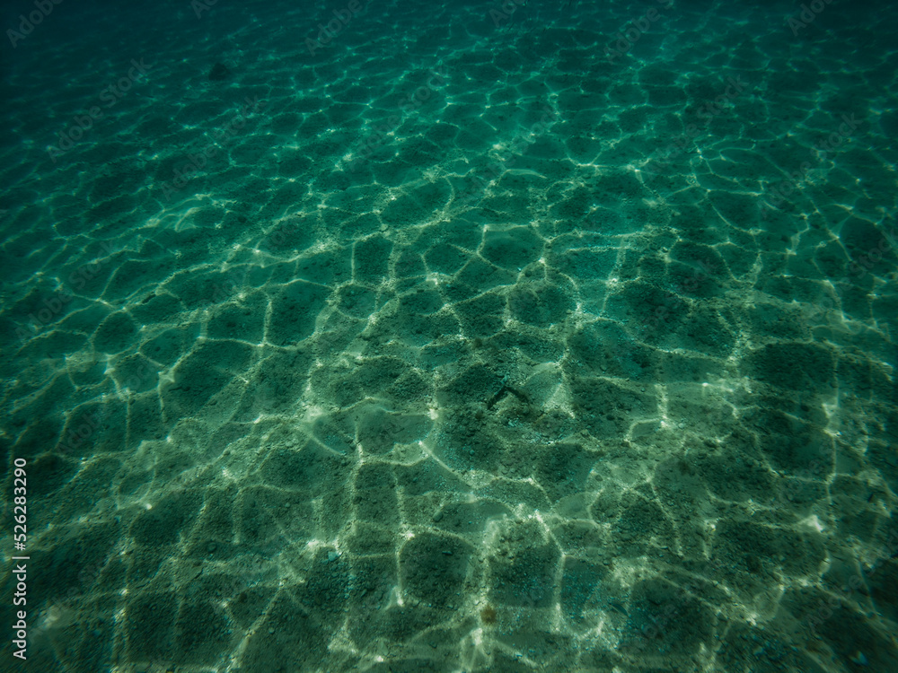 Underwater picture of sand sea bottom with waves refraction visible on the sea floor