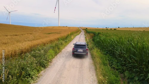 Farmer in grey car moves on road with beautiful landscape. Green corn field and wind turbines generating electricity. Concept of offroad travelling and active lifestyle. Go Everywhere for adventure photo