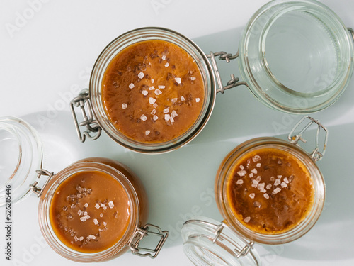 Salted caramel in glass jars, top view. Brown caramel or condensed milk with sea salt crystalls, shoot in bright or hard light. Light neutral background photo