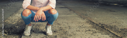 Detail of young girl crouching in torn jeans and sneakers