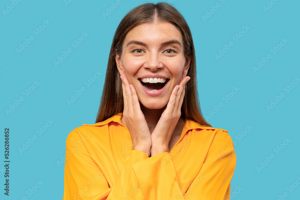Excited woman in yellow blouse surprised after hearing unbelievable news on blue background Excited woman in yellow blouse surprised after hearing unbelievable news on blue background