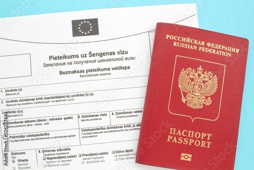 Schengen visa application form in Russian and Latvian language and passport on blue background. Prohibition and suspension of visas for tourists to travel to European Union and Baltic States concept