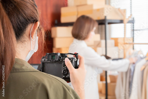 Selective focus of Asian vlogger woman influencer live streaming online for sale a clothes with digital camera, Small business owner, online market delivery concept. e-commerce and marketing media. © Rakchanok