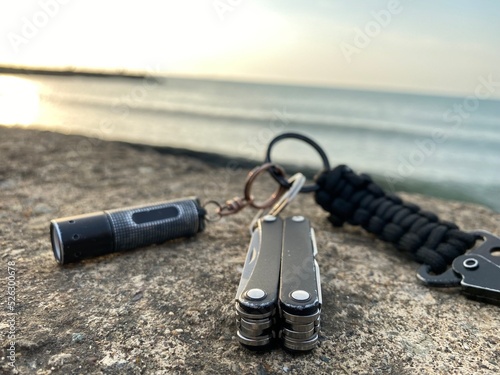 Pocket knife and flashlight on stone and sea background close up photo