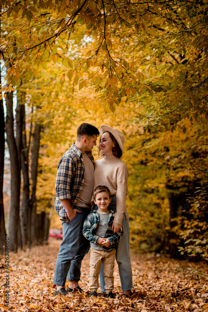 Portrait of happy young family on the background of autumn park. Mom, dad and son are smiling. Family autumn photo shoot