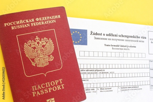 Schengen visa application form in Russian and Czech language and passport on yellow background. Prohibition and suspension of visas for Russian tourists to travel to Europe Union and the Baltic States