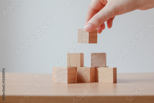Hand putting wood cube on top of wood block stacking as step stair. business growth to success.