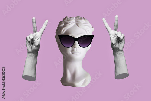Antique female statue's head in black sunglasses showing a peace gesture with hands isolated on a purple color background. Trendy collage in magazine surreal style. 3d contemporary art. Modern design photo
