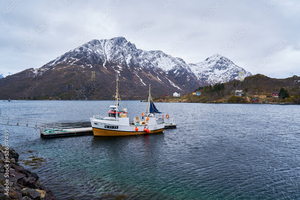 fishing boat moored in a Lofoten fjord with a snow-capped mountain behind it