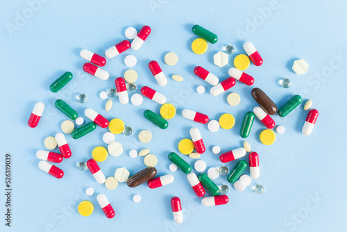 Pills of different shapes and colors are scattered on a blue background