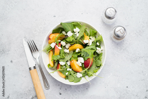 A light summer salad of rucolla, peaches and cheese spoon and knife on a light gray background. photo