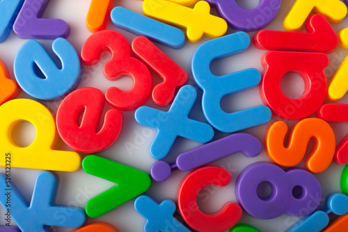 Plastic multi-colored alphabets letters on a magnet. Lots of сolorful letters scattered on a white background. The concept of elementary school background texture for children. Top view closeup.