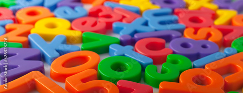 Plastic multi-colored alphabets letters on a magnet. Lots of сolorful letters scattered on a white background. The concept of elementary school background texture for children. Top view closeup.
