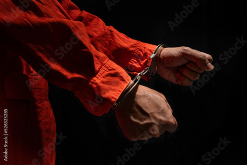 Handcuffs on Accused Criminal in Orange Jail Jumpsuit. Law Offender Sentenced to Serve Jail Time, in black background. photo