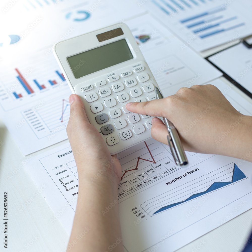 Accounting businessmen are calculating income-expenditure and analyzing real estate investment data, She works on a desk has graphs and calculators with laptop, Financial and tax systems concept. Accounting businessmen are calculating income-expenditure and analyzing real estate investment data, She works on a desk has graphs and calculators with laptop, Financial and tax systems concept.
