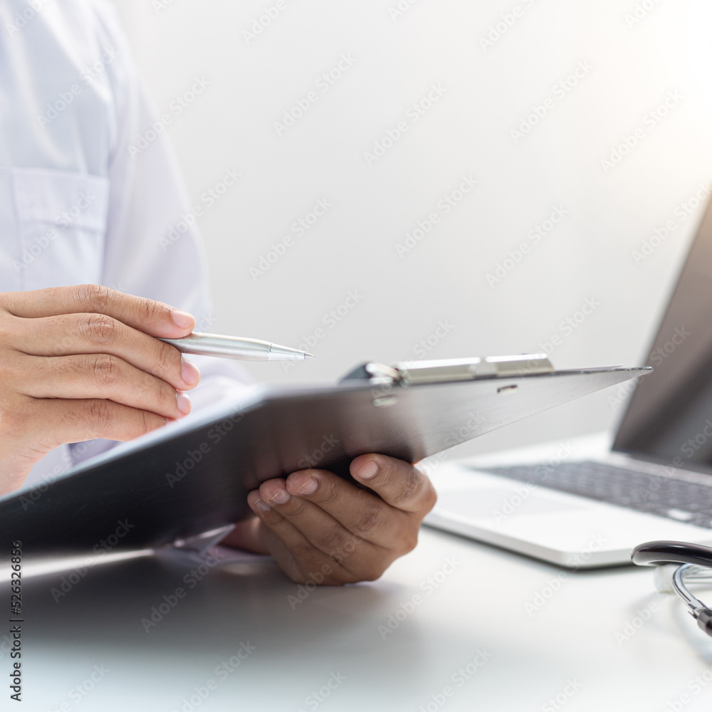 Doctor uses a laptop computer to record patient information and write it on a document to prepare for diagnosis in the room of a modern hospital, Emergency assistance and health care concept.