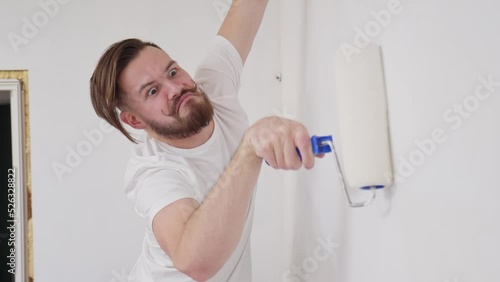 a young man with a funny mustache curled up paints the wall very diligently with a roller with white paint. the concept of home renovation, renovation in the apartment