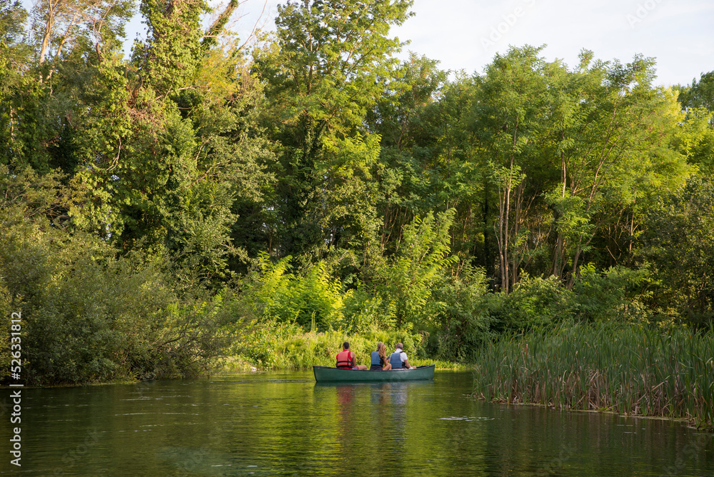 Couple having a canoe experience with a local guide on a natural blue river. Green landscape background Couple having a canoe experience with a local guide on a natural blue river. Green landscape background